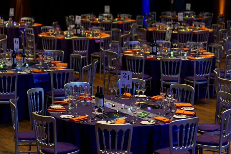 Round tables laid in blue and orange across the ballroom floor before the doors open.