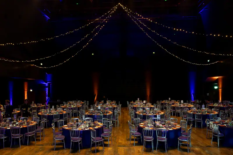 The ballroom before the guests arrive, tables laid under strings of warm lights.
