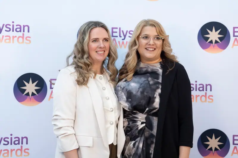 Two guests photographed together against the Elysian Awards backdrop.