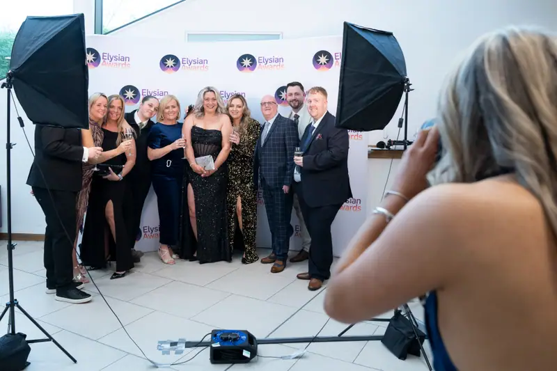 A group posing for the official photographer under studio lights at the Awards backdrop.