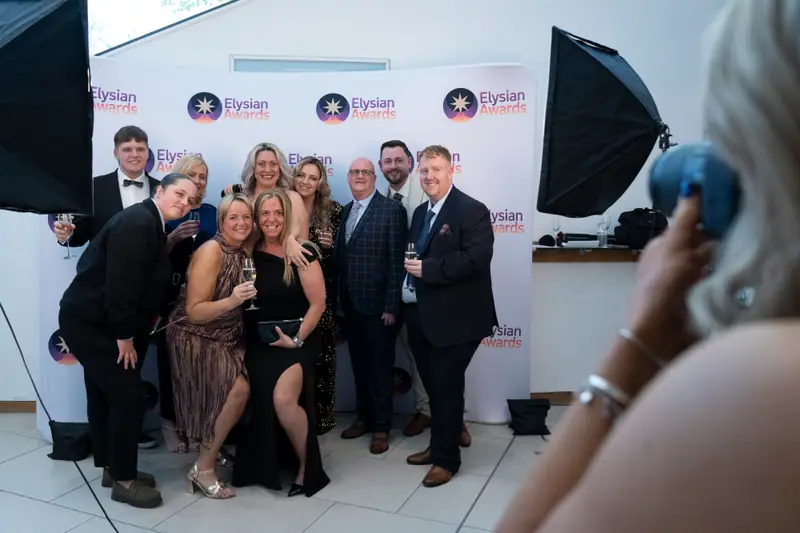 A table of guests crowding together for a photograph at the Awards backdrop.