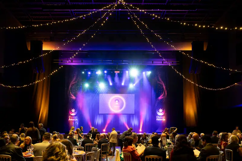 The full room watching the stage, lit purple and gold.