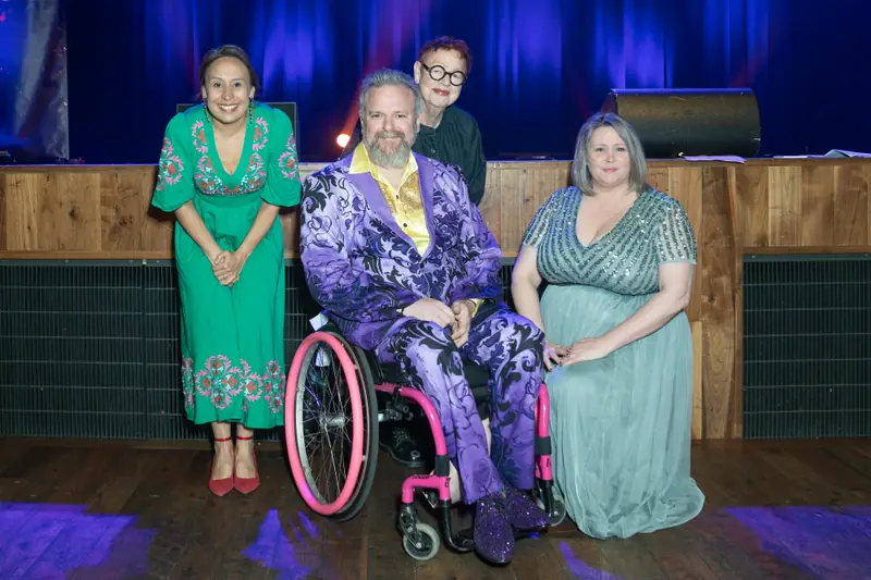Three winners together on stage, one using a wheelchair, holding their awards.