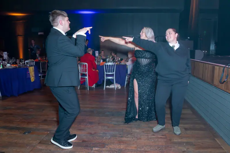 Three guests dancing, arms out, on the wooden floor.